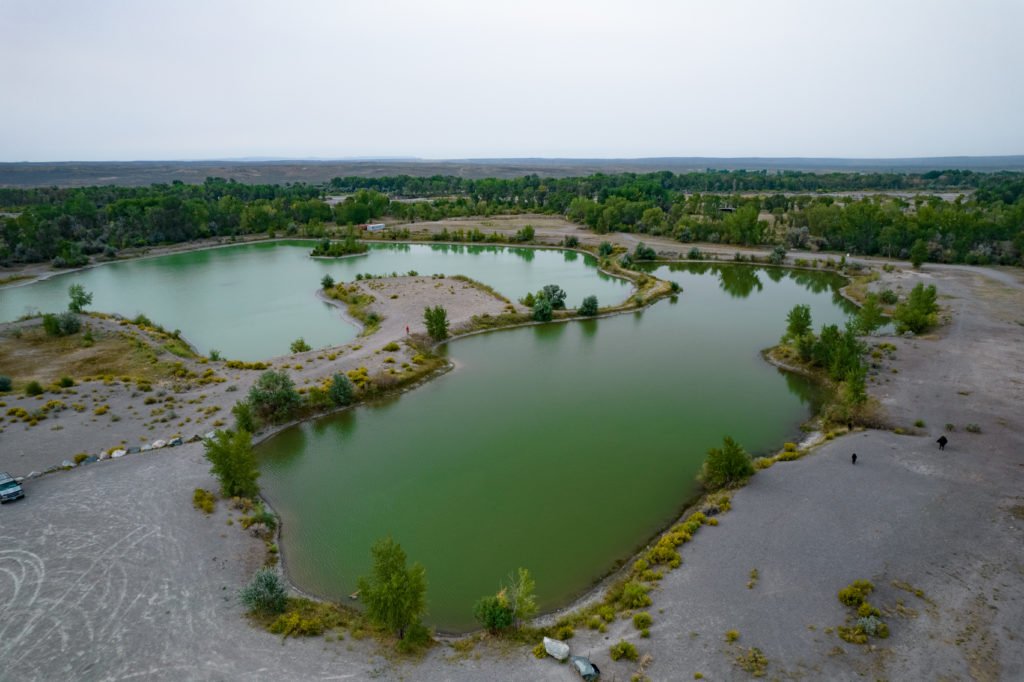 Aerial view of a serene landscape featuring interconnected green ponds surrounded by sandy terrain and lush vegetation in Wind River Country.