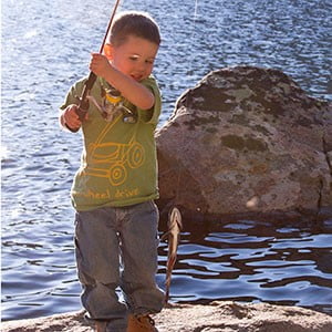 little boy holds up a fish on the shore of the reservoir