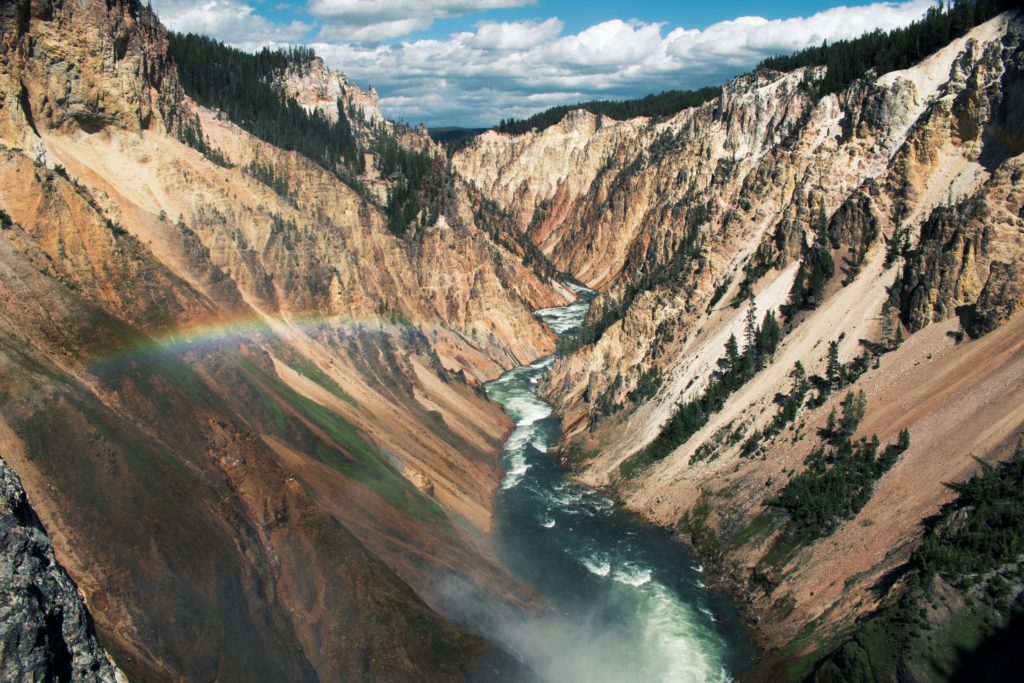 A majestic canyon with colorful rock layers, a winding river, and a vibrant rainbow arching across the sky in Wind River Country.