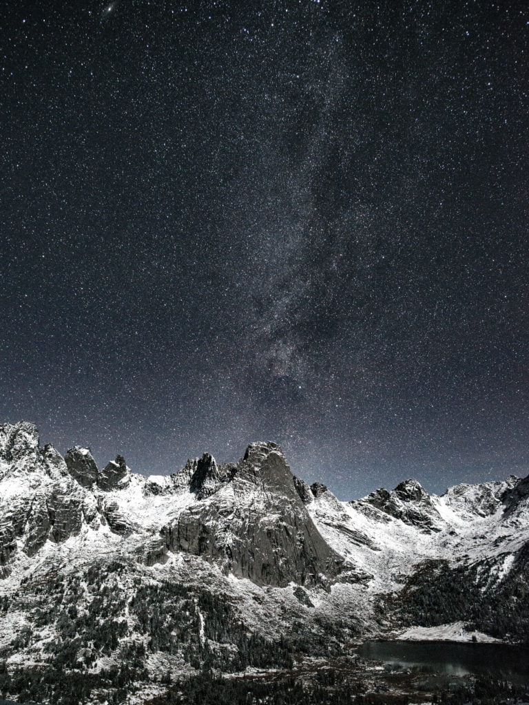 A breathtaking night view of snow-capped mountains under a starry sky with the Milky Way stretching across the horizon in Wind River Country.