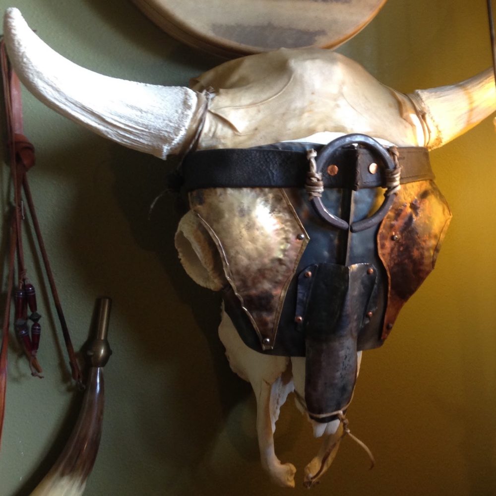 A decorative bull skull adorned with metal armor and a leather strap, mounted on a wall in Wind River Country.