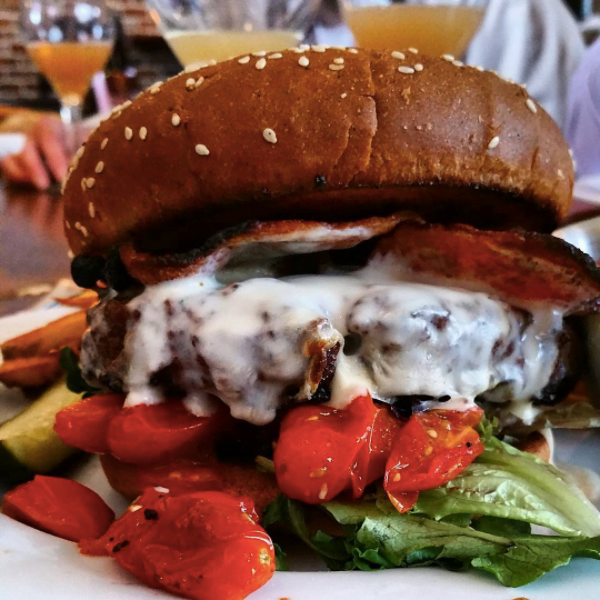 A mouthwatering cheeseburger topped with crispy bacon, roasted tomatoes, and lettuce on a toasted sesame seed bun in Wind River Country.