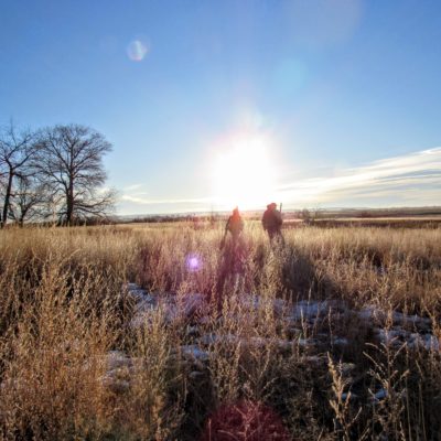Two hunters walk into the sun near Ocean Lake