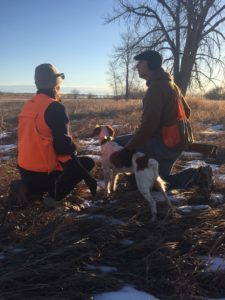 Two hunters with their dog pause to rest during a pheasant hunt