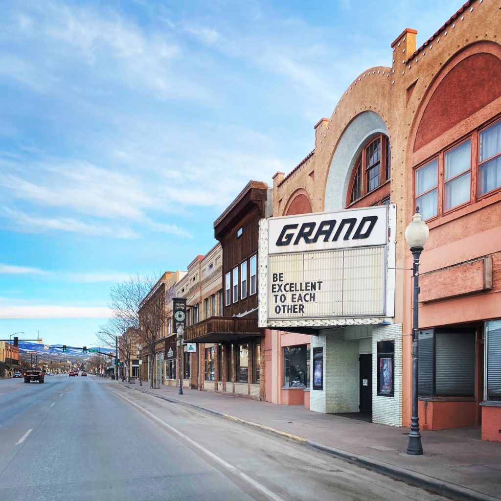 A quaint downtown street lined with historic buildings, featuring a prominent theater marquee that reads 'BE EXCELLENT TO EACH OTHER' in Wind River Country.