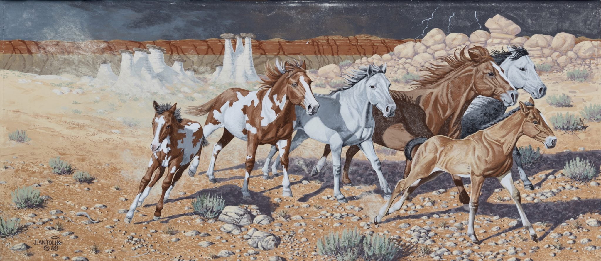 A herd of wild horses gallops across a desert landscape at sunset, with towering rock formations in the background in Wind River Country.