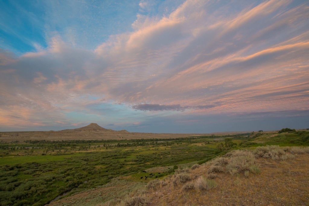 A vast, open landscape at sunset with rolling hills, a distant mountain, and a sky painted with hues of pink and purple in Wind River Country.