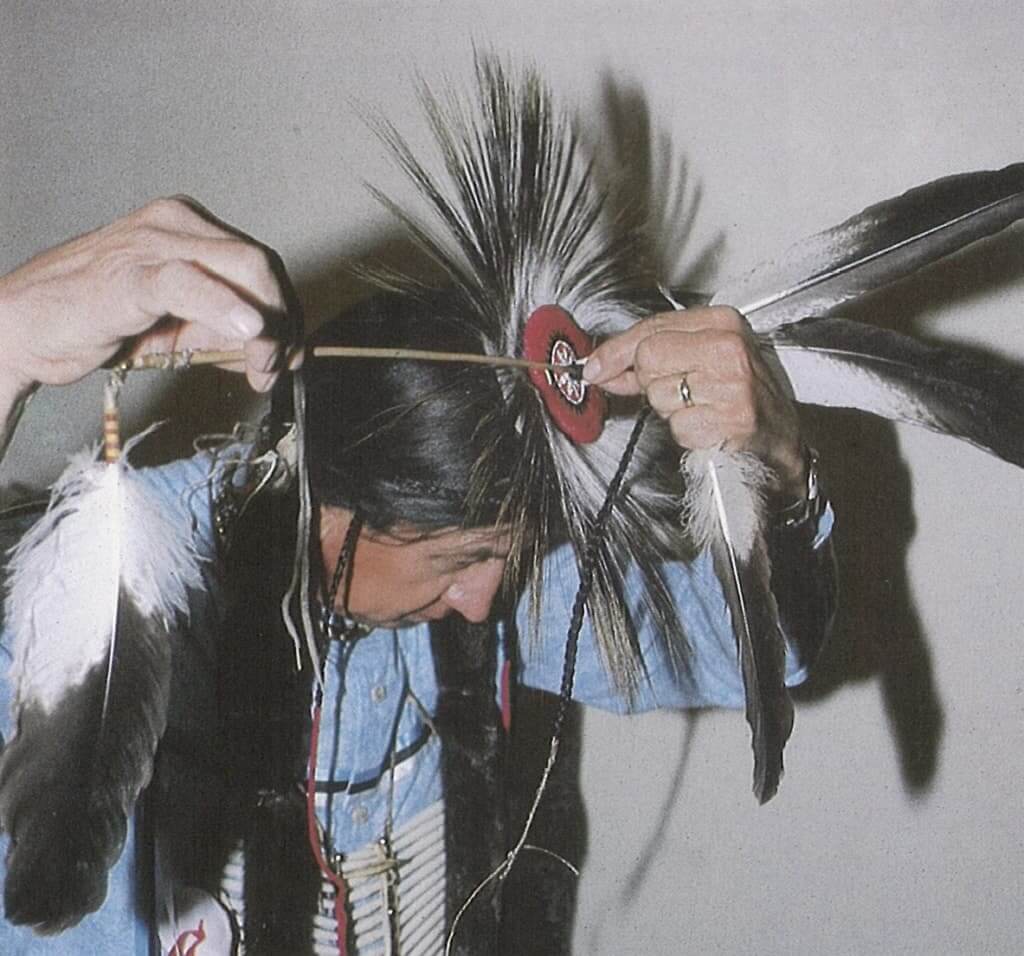 A person adjusting a traditional decorated stick on their head in Wind River Country.