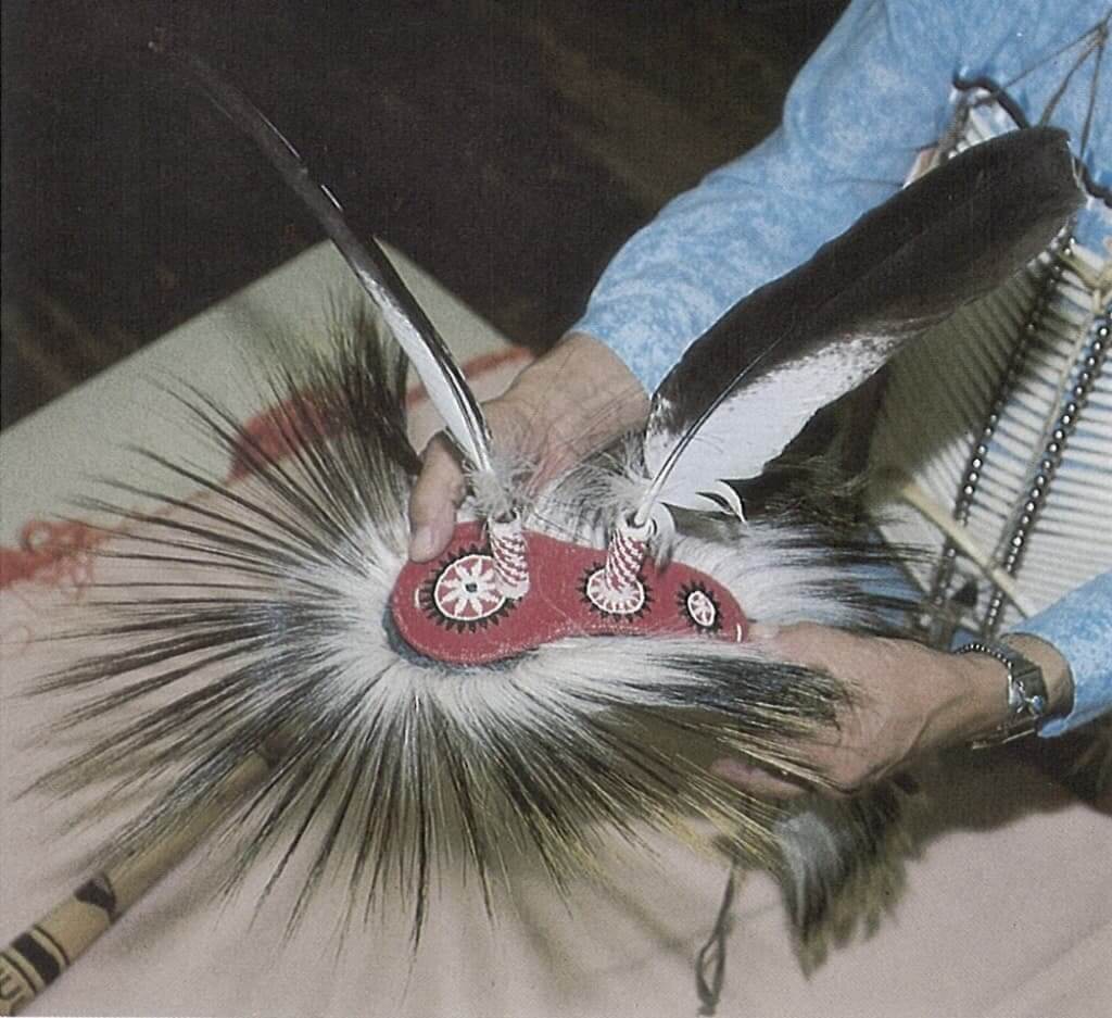 A person holding a traditional Native American roach headdress with feathers in Wind River Country-Spreader being positioned.