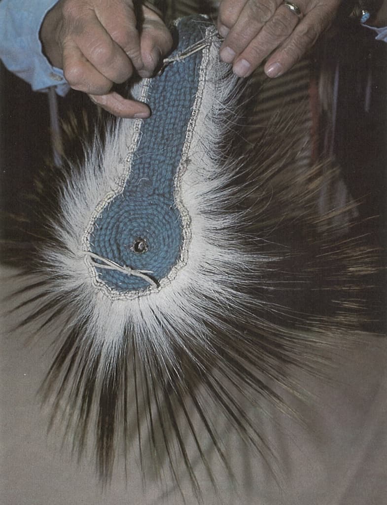 Hands holding a traditional Native American porcupine quillwork spreader with blue fabric in Wind River Country.