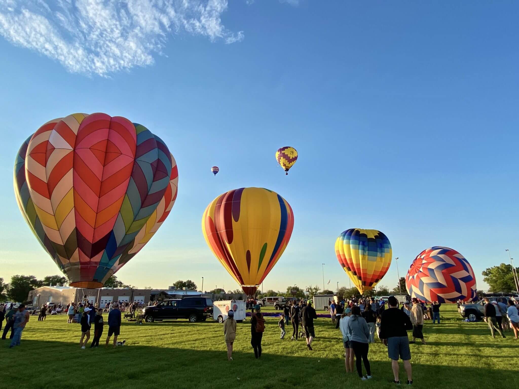 A vibrant hot air balloon festival with colorful balloons inflating on a grassy field, spectators gathered, and a clear blue sky overhead in Wind River Country.