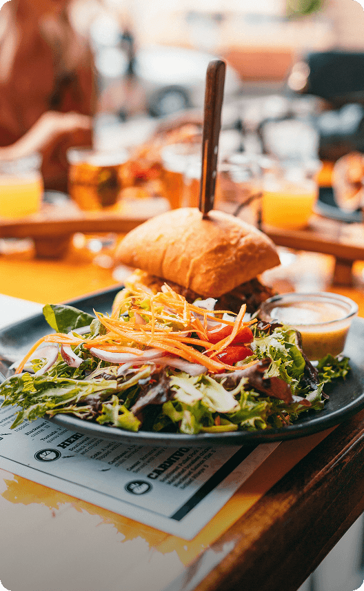 A mouthwatering burger with a side salad and a knife stuck in the bun, served on a sunny patio with drinks in the background in Wind River Country.