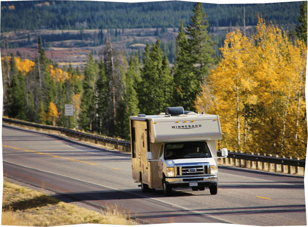 A Winnebago RV travels along a winding mountain road surrounded by vibrant autumn foliage in Wind River Country.