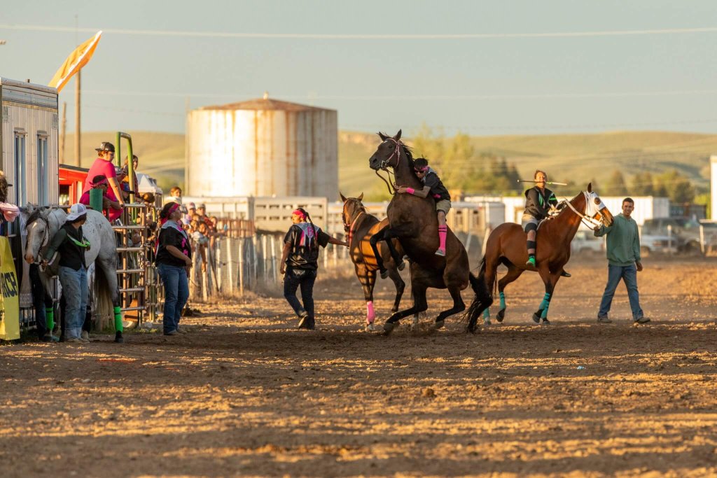 A thrilling horse race at a rodeo, with riders on bucking broncos and a crowd of spectators cheering them on in Wind River Country.
