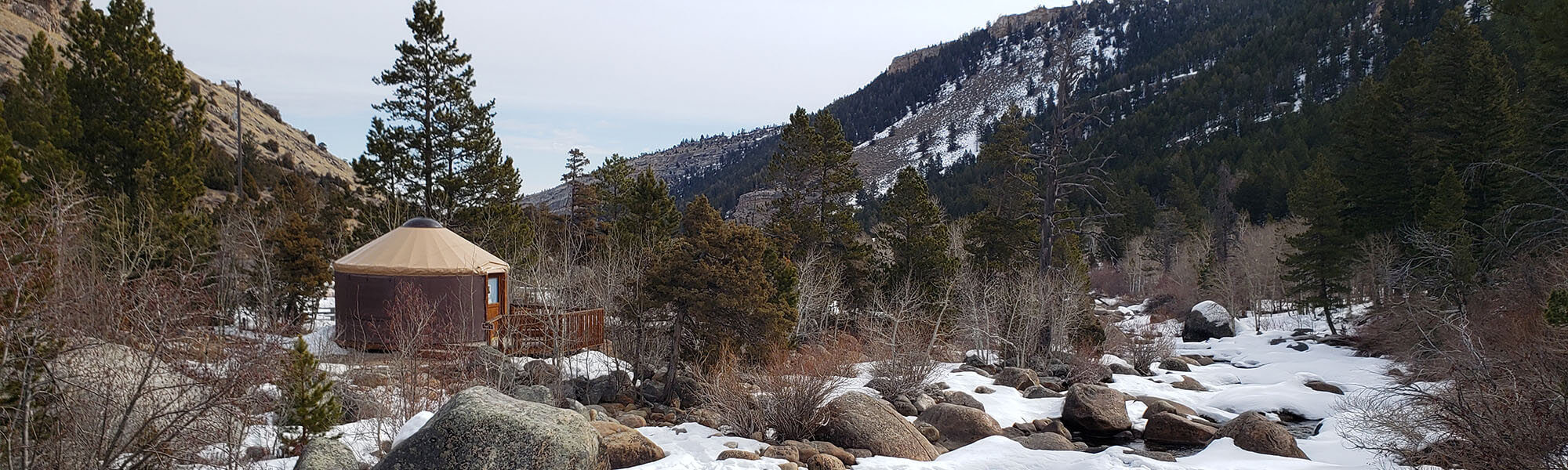 A cozy yurt nestled in a snowy mountain forest beside a frozen stream in Wind River Country.